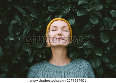 Portrait of relaxed and confident woman with eyes closed on background of green leaves wall. Thoughtful person in front of green hedge. Joy, zen and balance people. Stability through mental health Royalty-Free Stock Photo #2279564401