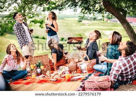 Fancy people laughing at vineyard place after sunset - Food and beverage concept with men and women drinking wine at barbeque party - Happy friends camping at open air pic nic on warm vivid filter Royalty-Free Stock Photo #2279576179