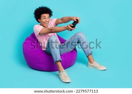 Full body photo of young professional console player funny chevelure sit beanbag gaming zone advert hold joystick isolated on blue color background