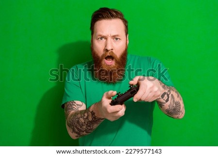 Portrait of masculine man red beard wear trendy t-shirt holding playstation joystick play excited game isolated on green color background Royalty-Free Stock Photo #2279577143