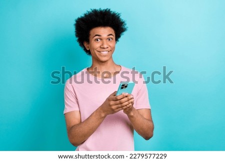 Portrait photo of young funny guy chevelure hairdo wear pink t-shirt hold his samsung galaxy phone browse website isolated on cyan color background