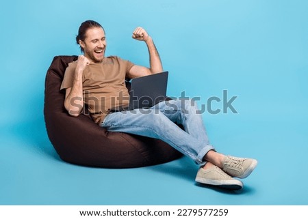 Full length photo of positive lucky guy dressed beige t-shirt bean bag winning game device empty space isolated blue color background Royalty-Free Stock Photo #2279577259