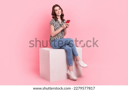 Full size photo of cheerful pretty girl sit podium use telephone chatting isolated on pink color background