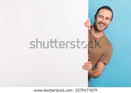 Photo of dreamy positive man wear beige t-shirt looking white poster emtpy space isolated blue color background