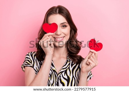 Portrait of pretty positive lady hold small red paper hearts cover one eye toothy smile isolated on pink color background