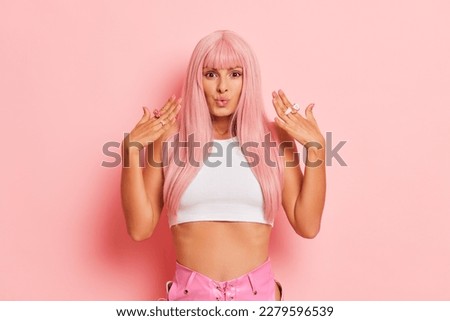 Close up of lovely young woman with long pink hair posing on pink background, gleefully whistles holding her palms near face, copy space, high quality photo