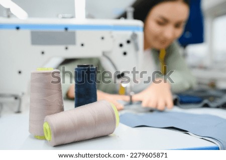 Young dressmaker woman sews clothes on working table. Smiling seamstress and her hand close up in workshop