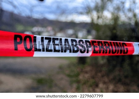 German crime scene or police barrier tape in a park saying 'Polizeiabsperrung', meaning Police cordon. 