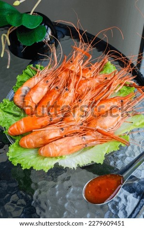 Boiled delicious king shrimps on green lettuce leaves with Thai sweet and sour sauce on a glass table. Close-up of seafood prawns