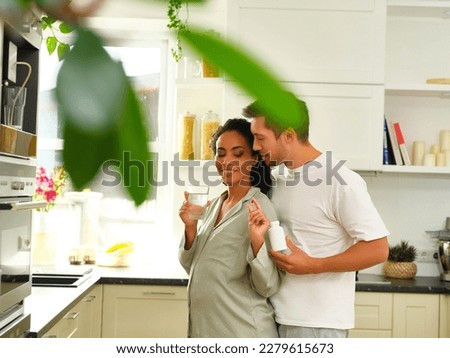 A man and a pregnant woman are taking vitamins or pills or a dietary supplement with a jar of vitamins and a glass of water in their hand, in a light kitchen Royalty-Free Stock Photo #2279615673