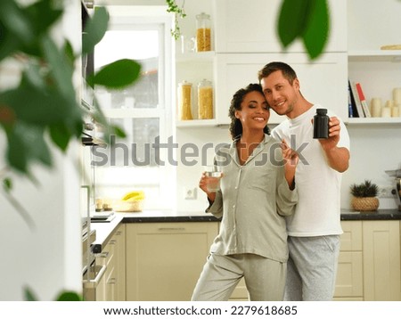 A man and a pregnant woman look at the camera while taking vitamins, pills, or dietary supplements, holding a jar of vitamins and a glass of water in their hands Royalty-Free Stock Photo #2279618685