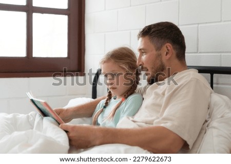 Little girl's father read stories to children before going to bed to unwind and sleep soundly until the morning.