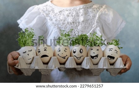 Funny easter eggs with different painted mines in a cartoon holding by hands of girl. Green watercress sow and grow in eggs in spring. Banner.
