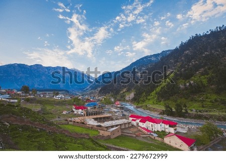 The landscape picture of houses in the mountains of Kalam, Pakistan. The image captures a serene and tranquil setting that is surrounded by lush green forests and lake.