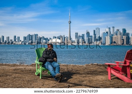 man sitting on chair and smiling on the coast of toronto island park with toronto skyline on background