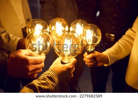 Business team sharing creative energy and developing new ideas. Group of people holding bright glowing electric Edison light bulbs as symbol of idea and innovation. Lightbulbs in human hands, close up Royalty-Free Stock Photo #2279682589