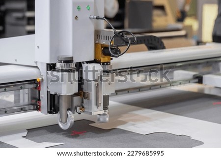 Digital flatbed cutter, plotter cutting white cardboard sheet at printer exhibition, trade show - close up. Technology, industrial, manufacturing, robotic, electronic concept