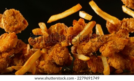 Freeze Motion Shot of Flying Fresh Fried Chicken Wings or Strips with French Fries, Close-up