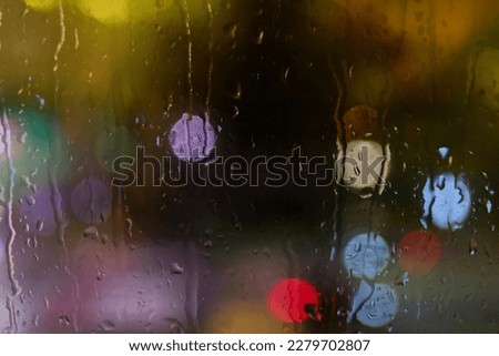 Looking outside trough a rainy window with blurred lights in the background 