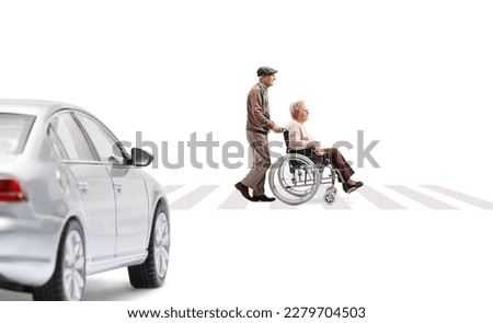 Full length profile shot of an elderly man pushing an elderly woman in a wheelchair at a pedestrian crossing and car waiting isolated on white background