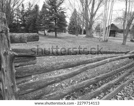 black and white photo of a old wooden fence with trees and a old barn in background.