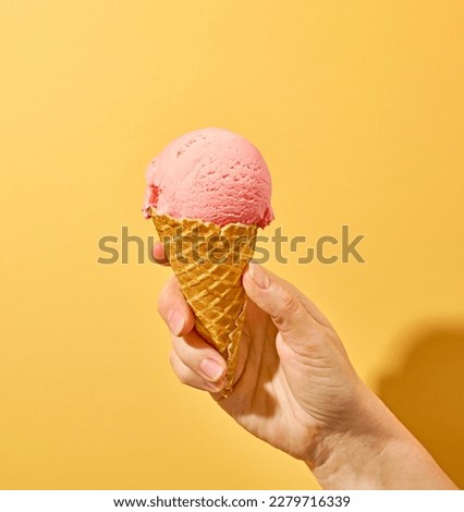 pink ice cream in human hand on yellow background