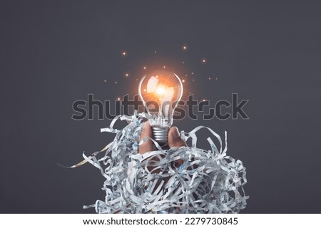 Light bulb and pile scrap paper from shredder on table desk (Text appears is in Thai characters which can't translate because it was cut off, damaged by the document shredder.) For recycle concept.