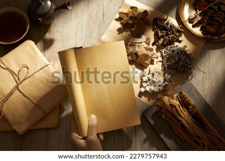 A hand model holding ancient Chinese medicine books with many types of herb, medicine packs, a bowl of medicine and earthen pot displayed behind. Herbal medicine is safe and easy to use Royalty-Free Stock Photo #2279757943