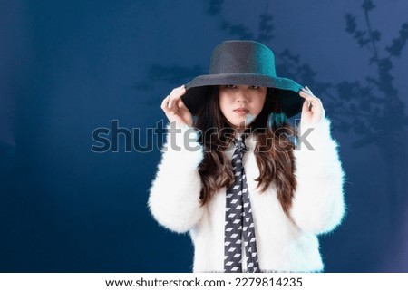 Portrait of cheerful beautiful Asian curly girl in white fur coat over blue background.
