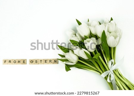 Bouquet of white tulips with a white bow on the right in the picture on a white background, on the left the words HAPPY EASTER in german with wooden game pieces, free space at the top left, horizontal