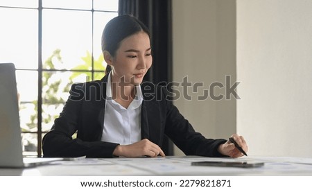 Professional businesswoman in  elegant suit sitting at office desk checking financial reports.