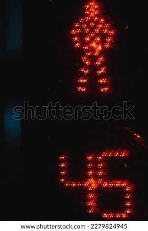 Pedestrian crossing traffic light with timer shows red stop signal with LED man sign over black night background, close up vertical photo