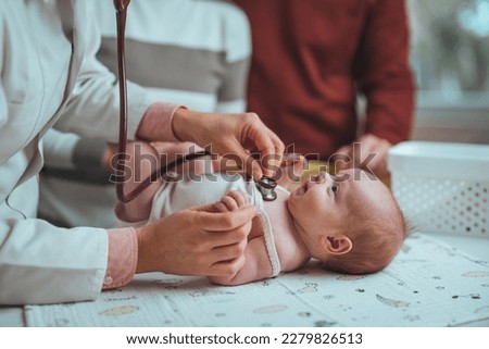 Newborn lying on back while doctor listening to his heartbeat with stethoscope at hospital. Close up of unrecognizable doctor examining cute baby lying on changing table in clinic, copy space Royalty-Free Stock Photo #2279826513
