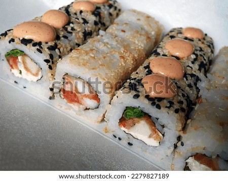 Sushi rolls with fish and cheese, sesame seeds and sauce close-up on the table.