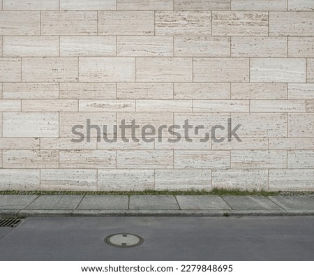 image of a tiled beige stone wall a sidewalk and a street as background, natural stone wall texture as background. Close-up of a wall clad in limestone Royalty-Free Stock Photo #2279848695