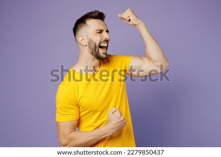 Young overjoyed happy fun caucasian man wear yellow t-shirt doing winner gesture celebrate clenching fists say yes isolated on plain pastel light purple background studio portrait. Lifestyle concept Royalty-Free Stock Photo #2279850437