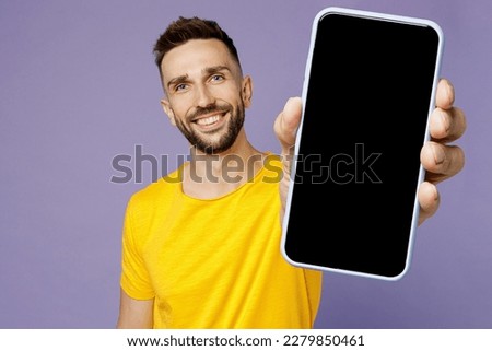 Young fun man wear yellow t-shirt hold in hand use show close up mobile cell phone with blank screen workspace area isolated on plain pastel light purple background studio portrait. Lifestyle concept Royalty-Free Stock Photo #2279850461