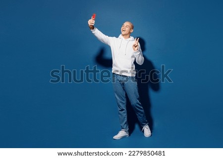 Full body young man of African American ethnicity wear white hoody do selfie shot on mobile cell phone post photo on social network isolated on plain dark royal navy blue background studio portrait