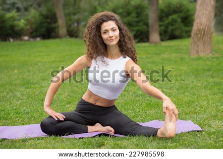 Pretty woman doing yoga exercises in outdoor park setting, green grass background