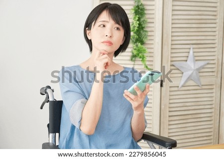 Asian woman in a wheelchair using a smartphone in the living room