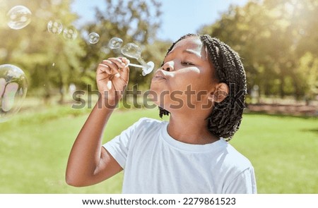 Park, child and black girl blowing bubbles enjoying fun time alone outdoors, joy and childhood development. Happy, freedom and kid learning and playing with soap bubble toy or wand and relax on grass Royalty-Free Stock Photo #2279861523