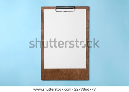 New wooden clipboard with sheet of blank paper on light blue background, top view