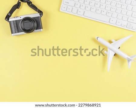 Top view or flat lay of airplane model, computer keyboard, and digital camera with copy space on yellow background, business and traveling concept.