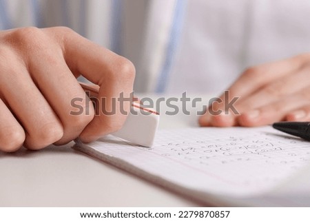 Girl erasing mistake in her notebook at white desk, closeup Royalty-Free Stock Photo #2279870857