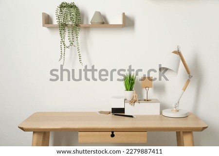 Comfortable workplace with wooden desk near white wall Royalty-Free Stock Photo #2279887411