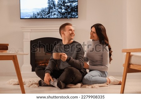 Happy lovely couple with hot drinks spending time together near fireplace at home