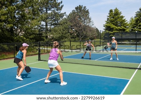 A competitive doubles game of pickleball at the net on a blue and green court in summer. Royalty-Free Stock Photo #2279926619