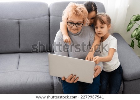 grandmother and two granddaughters use laptop at home