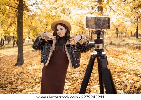 Style woman using smartphone with stabilizer, taking pictures and live video in autumn city park. Vlog, video blogging, outdoor photography concept. copy space