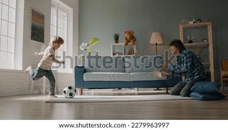 Funny father and son playing football at home. Little caucasian kid kicking the ball while his positive father catches it - active games, happy family, togetherness  Royalty-Free Stock Photo #2279963997